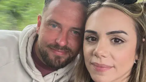 Jason and Mimi take a selfie while sat on a train, their heads touching.