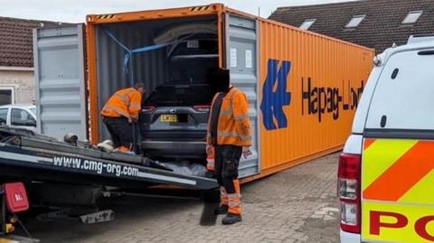 Officers examining stolen cars inside an orange  container 