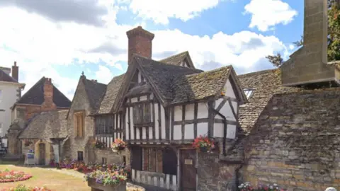 The Almonry is pictured. It is a historic 14th-century building tudor-style building, with white, black and sandstone facade.