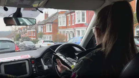 Paramedic Nicola Hughes sits in a response car and holds a two-way radio.