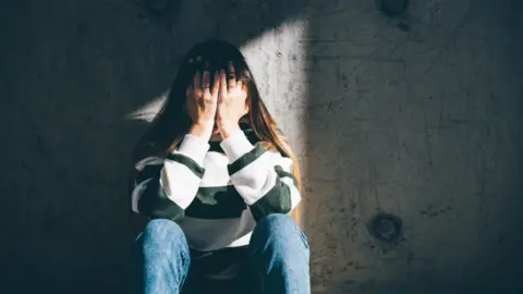 Getty Images Young woman holding head in hands against concrete wall (stock image)