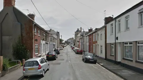 A row of painted terraced houses with cars lining either side of the road