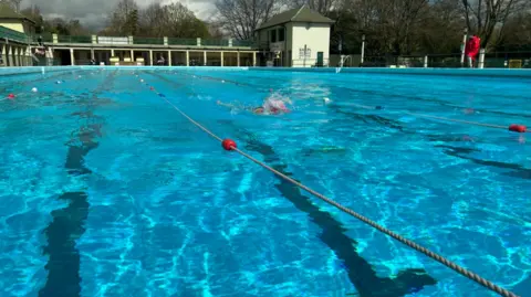 Swimming pool with blue water and some people swimming in it - set within a green building 