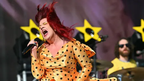 Getty Images The singer CMAT performs onstage at the TRNSMT music festival. She has a yellow dress with polka dots on and is singing into the microphone with energy.