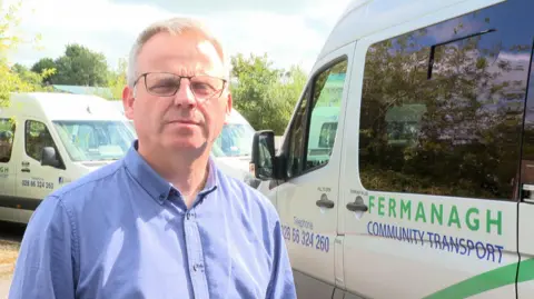 Jason Donaghy wearing glasses and a blue shirt, standing beside a Fermanagh Community Transport vehicle