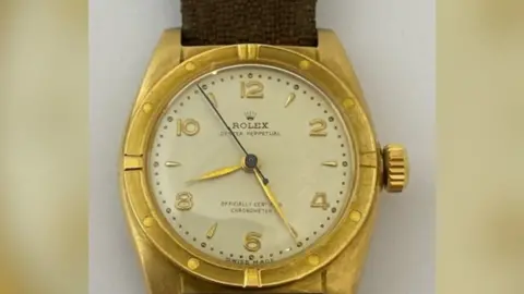 A close up image of an 18ct gold Rolex watch face with a brown canvas strap.