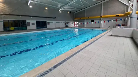 A wide photo of a corner of a swimming pool, taken from the side with tiled flooring in the background.
