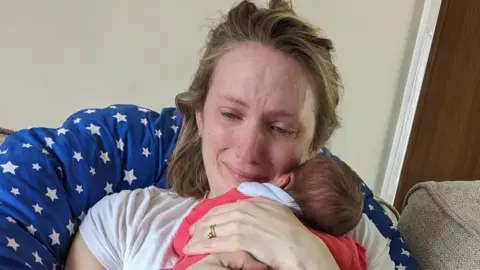 Louise cuddles her newborn baby, while she is crying