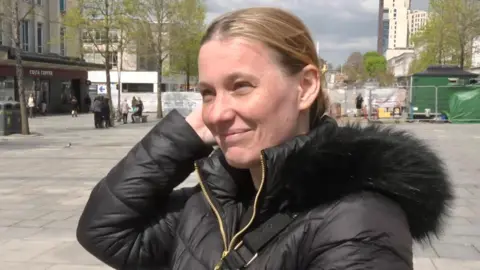 Jenni Massey is wearing a black hooded jacket with a fur collar and a cross-shoulder bag and is in Armada Way in Plymouth with redevelopment works going on behind her