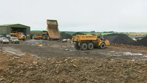 BBC Dump trucks moving coal at Bradley Surface Mine. Piles of coal stand in the background.