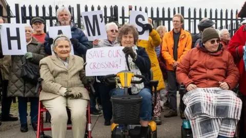 Jean Dixon A group of about 17 people who were part of a larger protest against the crossing closure. Three people at the front of the group are in wheelchairs.