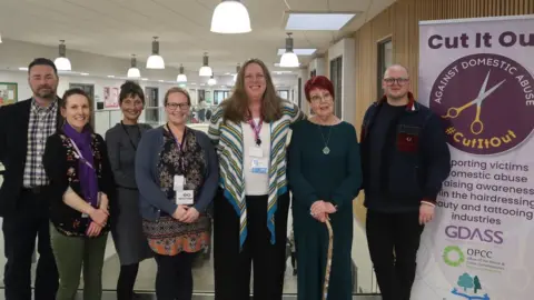 Forest of Dean District Council Seven people smiling at camera next to poster reading Cut it Out