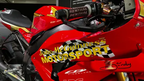 A red bike with yellow logos mirroring the 1996 machine.