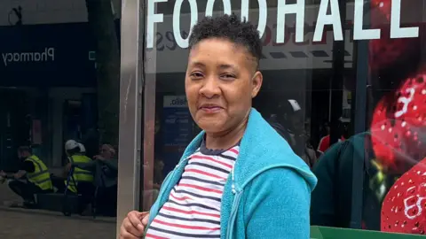 Woman looking into camera while standing outside M&S shop with an M&S bag in her hand.