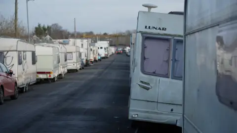A road with caravans parked along on each side of it. The caravans stretch as far as the eye can see.