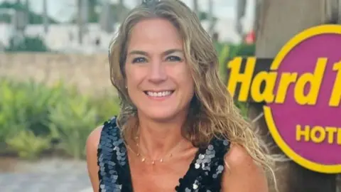 A woman in a black sequinned top on holiday against a Hard Rock sign