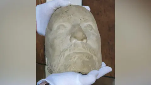 Visit Worcestershire A beige stone mould of a man's face, being held by someone wearing white gloves.