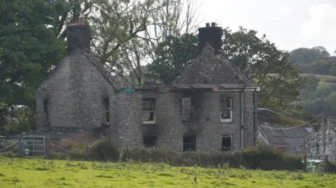 BBC A burnt down two story house next to a farmhouse in a field 