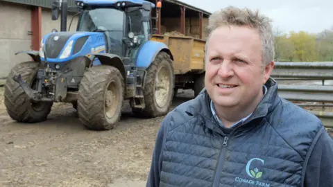 Tom Collins stood in front of a tractor on a farm.