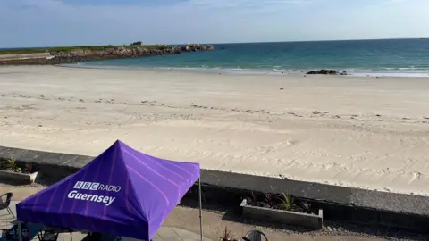 BBC A sandy Pembroke Bay, with the tide a third of the way up the shore, with a purple BBC Radio Guernsey tent in the foreground.