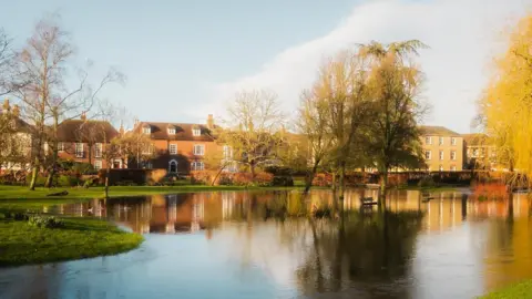 WeatherWatchers/Tom Pollard Photography The sun sets in Salisbury town centre, with flood water reflecting the trees and historic buildings in the background.