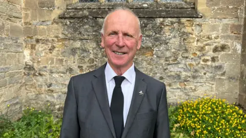 Dennis William Brown wearing a suit and stood outside the stone church