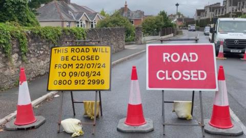 Road with road closed sign and three traffic cones 