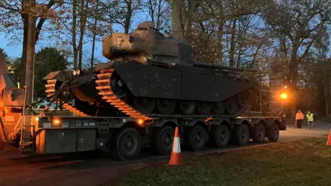A green painted tank sitting on a military lorry arriving at Thoresby at dusk
