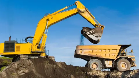 Getty Images A digger unloads earth into a large dumper truck on a building site