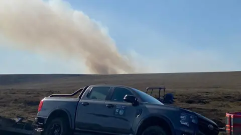 DFRS A truck near moorland in the Peak District where a plume of smoke can be seen in the distance on Friday 1 May 2026 from the wildfire off the A57 Snake Pass, near Glossop, Derbyshire.