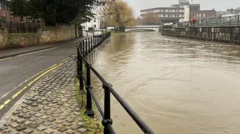 A brown river very close to spilling onto a road.