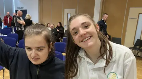 Amy (left), with dark hair, wearing a black hoodie jacket, beside Sasha, who has a white shirt and brown hair.