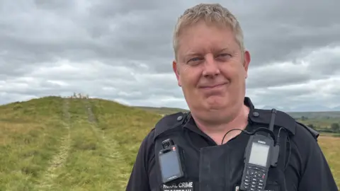 PC Dave Allen smiling at the camera in front of the burial mound