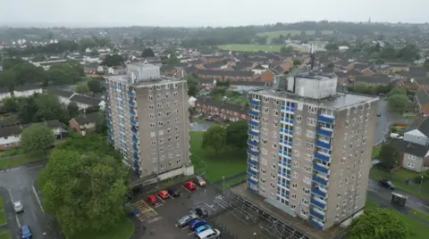 Tower blocks surrounded by a car park and trees and green space.