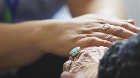 Close up of health care worker holding hands with senior woman at home - stock photo