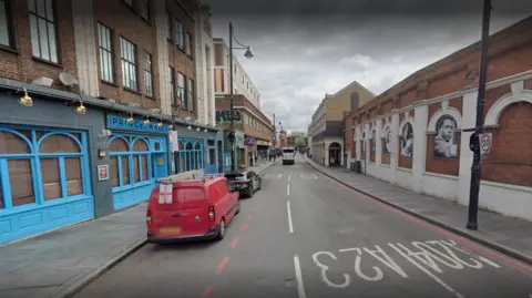 Brixton Road street view shows two parked cars in front of blue Prince of Wales pub and a wall with portraits on the right