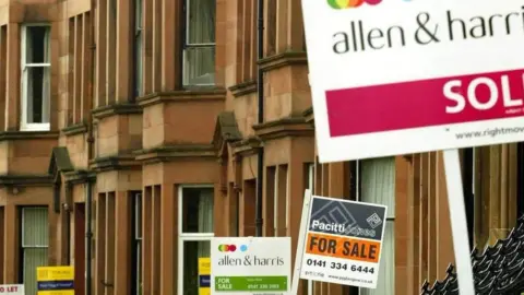 PA Media A close up of a row of red/brown sandstone houses with placard for sale signs for different estate agents in the street