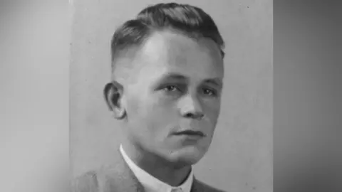 David Wilkins A black and white portrait photo of Private Ray Bailey wearing a suit. He has short tidy hair and looks very young. 