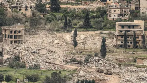 AFP A photograph taken from northern Israel shows Israeli military armoured vehicles driving past destroyed buildings across the border in southern Lebanon (15 April 2026)