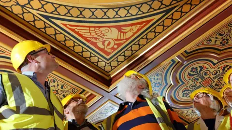 Maison Dieu People in hard hats looking at a ceiling with a dragon design.