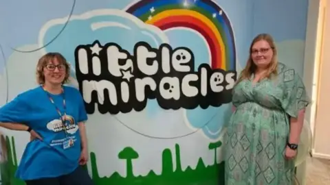 Louise and Michelle King standing in front of a little Miracles board 