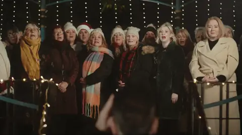 North Northamptonshire Council A large group of female carol singers standing and performing in a variety of winter attire.