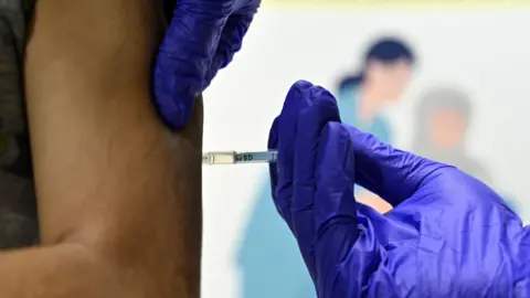 A person's hand held by a medical profession wearing blue gloves and holding a needle