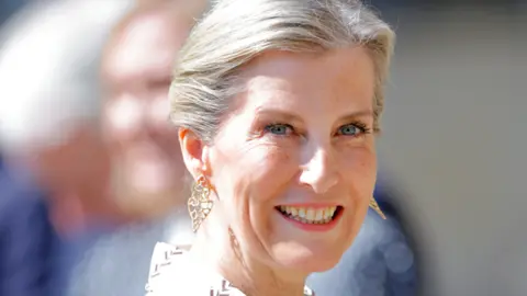 A woman with short blonde hair and a gold earring