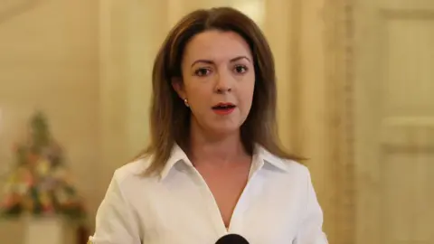 PA Media Liz Kimmins, with long brown hair, wearing a white shirt. 