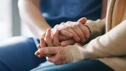 Getty Images An elderly woman's hands and a carer's hands placed on top of each other 