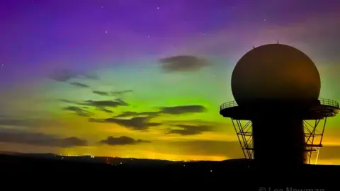 Lee Newman The Northern Lights captured over Clee Hill, with the main radome in Silhouette against the sky, which is purple, green and yellow