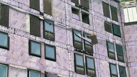 A large purple building with some loose covering hanging on the edge of the building.