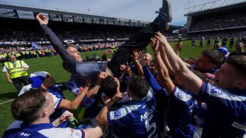 Rex Features Kieran McKenna being held aloft on the pitch at Portman Road by a large group of Ipswich Town players who are all wearing blue Ipswich Town shirts