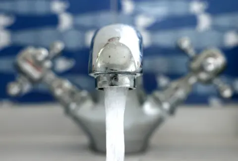 A stainless steel tap with water flowing from its faucet. 